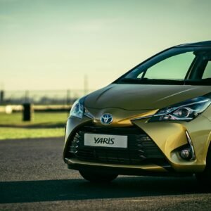 Sleek yellow Toyota Yaris parked on a sunlit asphalt road outdoors.